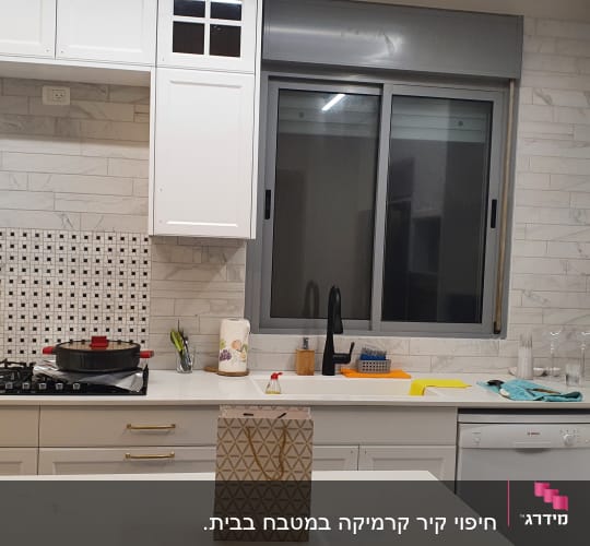 מטבח עם ארונות לבנים, כיור וברז שחור, כיריים וגז